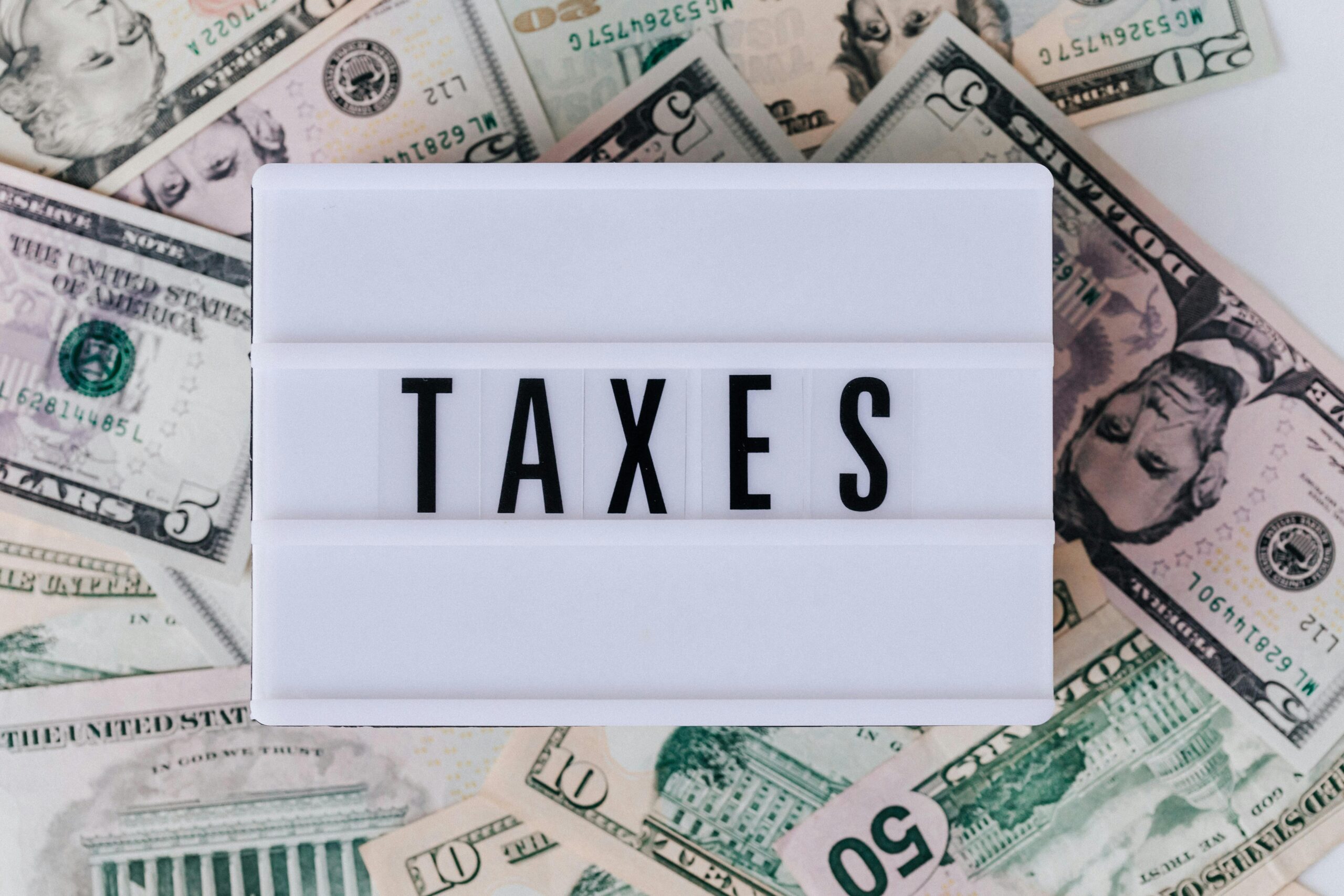 Top view of white vintage light box with TAXES inscription placed on stack of USA dollar bills on white surface. into to taxes, understanding taxes